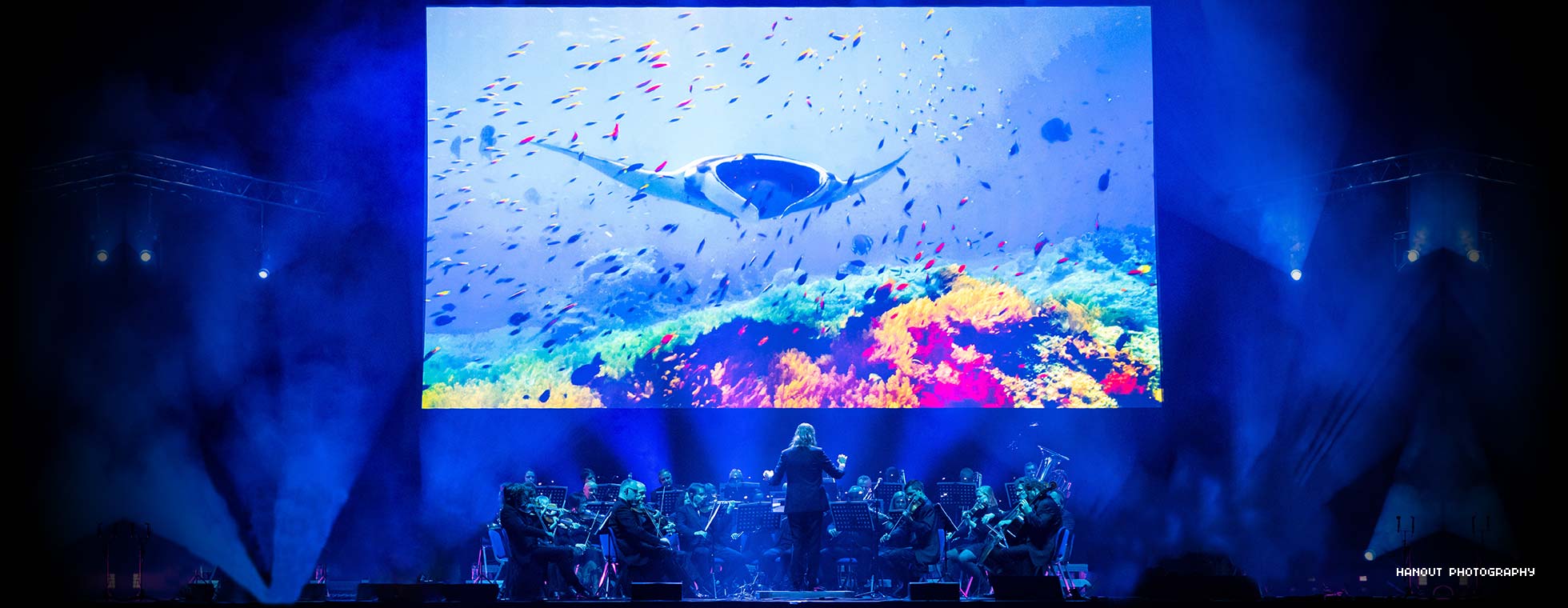 Orchestra concert on stage with ocean footage on a screen behind them