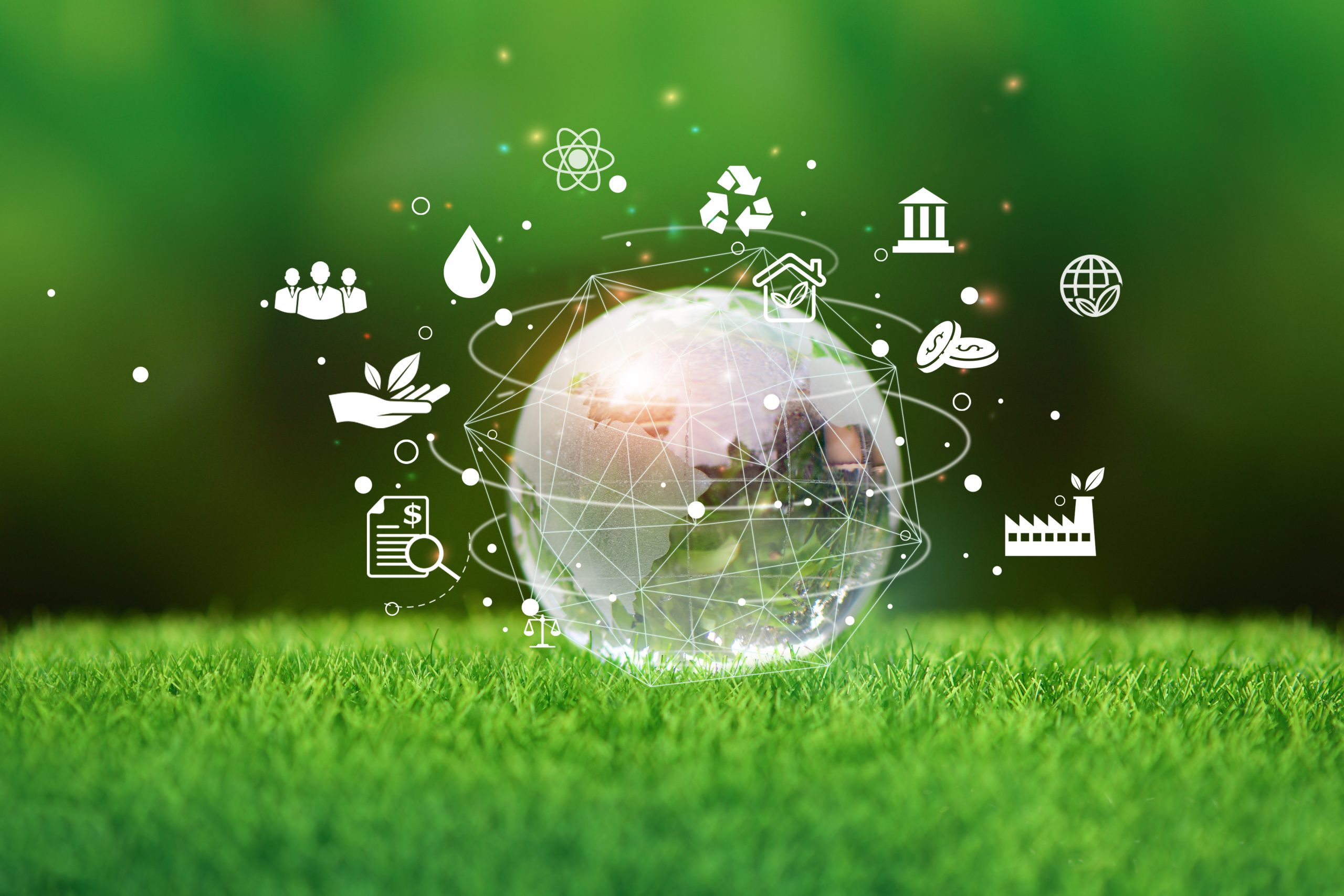 Stock photo of glass earth sitting on green grass with icons representing aspects of sustainability circling it