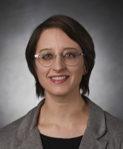 Photo of Christine Costello wearing clear-rimmed glasses, a dark tan/gray blazer and black top.