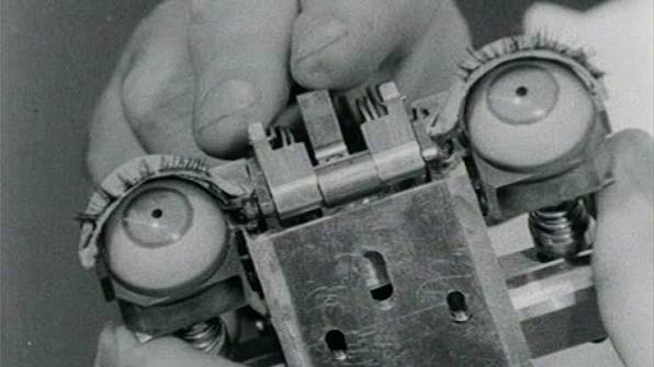 Still image from the film "Ghost in the Machine" that shows a rudimentary robot's eyes held by a human hand